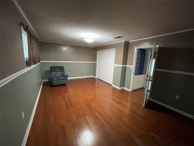 interior space featuring ornamental molding, visible vents, a textured ceiling, and wood finished floors