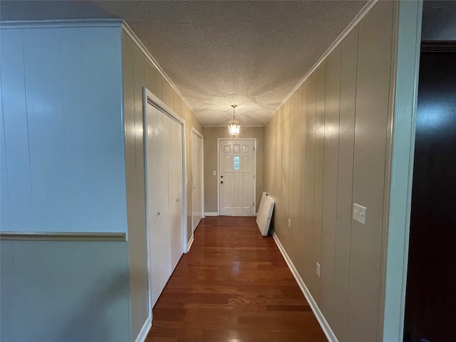 hallway featuring ornamental molding, a textured ceiling, wooden walls, and dark hardwood / wood-style flooring