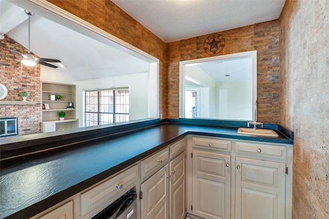 kitchen with sink, vaulted ceiling, ceiling fan, a fireplace, and white cabinetry