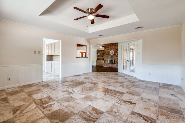 unfurnished living room with a tray ceiling, ceiling fan, ornamental molding, and a brick fireplace