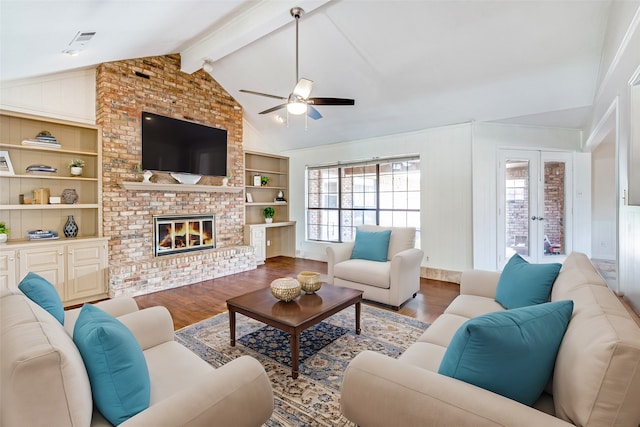 living room featuring ceiling fan, built in features, a fireplace, hardwood / wood-style floors, and vaulted ceiling with beams