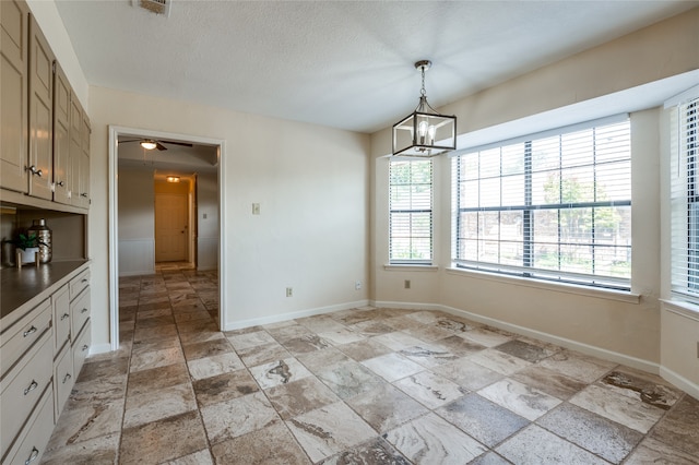 unfurnished dining area featuring ceiling fan with notable chandelier and a textured ceiling