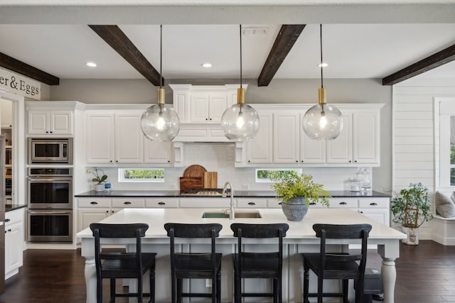 kitchen with beamed ceiling, dark hardwood / wood-style floors, hanging light fixtures, and a center island with sink