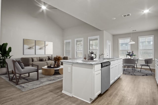 kitchen with light hardwood / wood-style flooring, a kitchen island with sink, stainless steel dishwasher, hanging light fixtures, and white cabinets