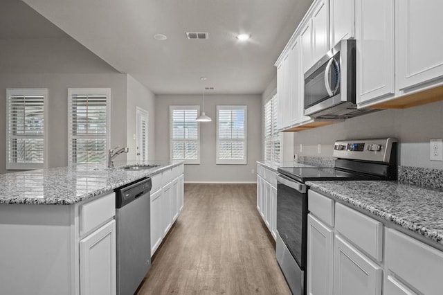 kitchen with hardwood / wood-style floors, stainless steel appliances, white cabinetry, sink, and a kitchen island with sink