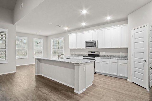 kitchen featuring a kitchen island with sink, stainless steel appliances, wood-type flooring, light stone counters, and white cabinets