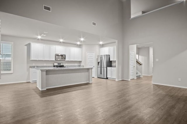 kitchen with an island with sink, hardwood / wood-style floors, stainless steel appliances, and white cabinets