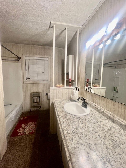 bathroom with heating unit, bathtub / shower combination, vanity, wood walls, and a textured ceiling