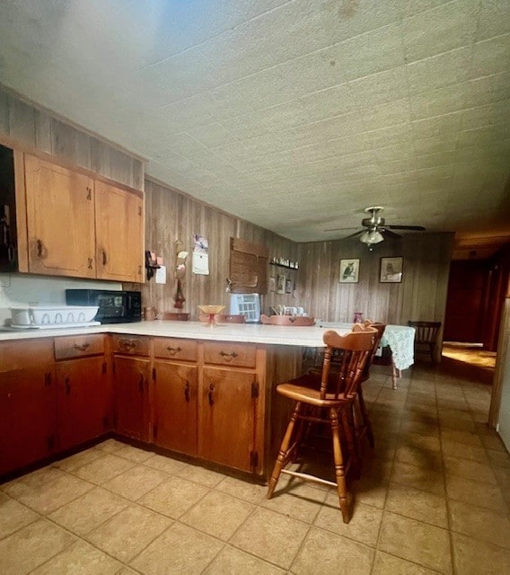 kitchen featuring kitchen peninsula, light tile patterned flooring, wood walls, ceiling fan, and a kitchen bar