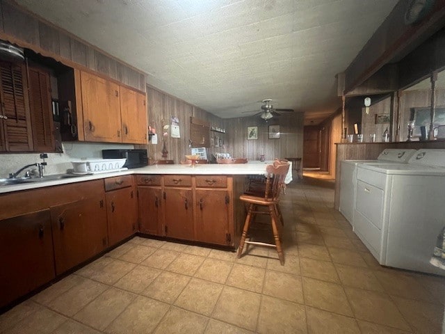 kitchen featuring a breakfast bar area, light tile patterned floors, independent washer and dryer, kitchen peninsula, and ceiling fan