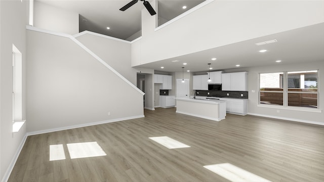 unfurnished living room featuring ceiling fan, light hardwood / wood-style floors, a towering ceiling, and sink