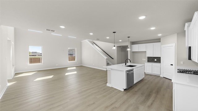 kitchen featuring decorative light fixtures, white cabinetry, light hardwood / wood-style floors, sink, and a center island with sink