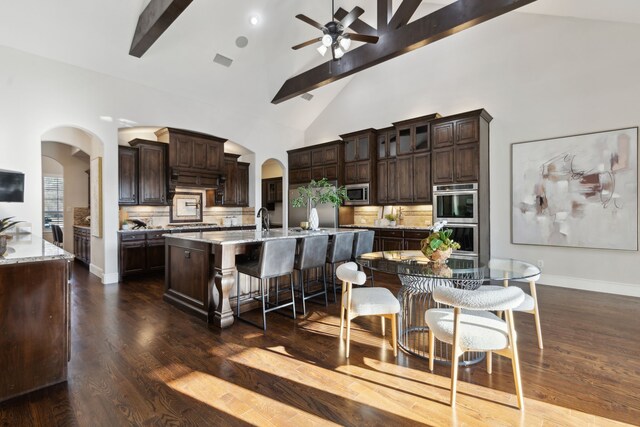 kitchen featuring arched walkways, decorative backsplash, a large island, appliances with stainless steel finishes, and a kitchen breakfast bar