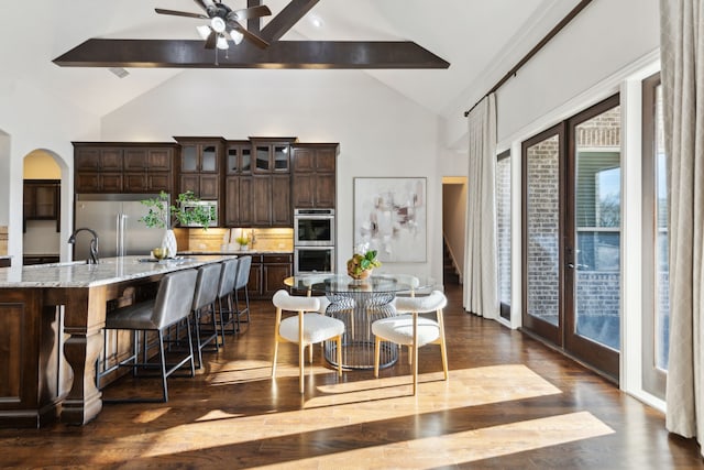 dining area featuring dark wood-type flooring, ceiling fan, beam ceiling, arched walkways, and high vaulted ceiling