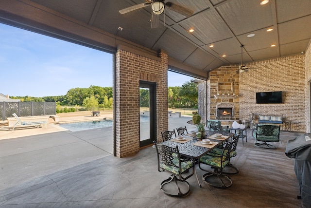 view of patio / terrace with a fenced in pool, a lit fireplace, and a ceiling fan