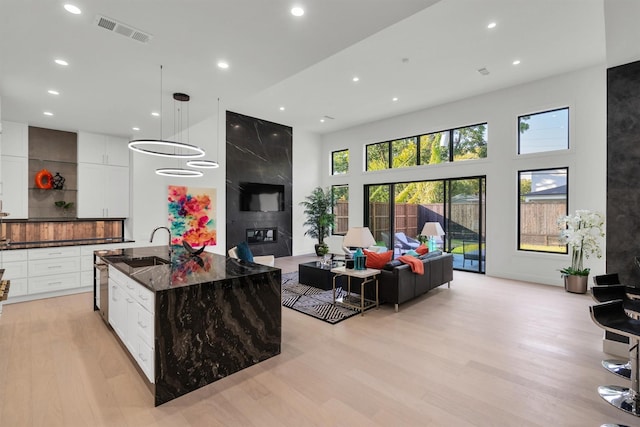 kitchen featuring pendant lighting, dark stone counters, an island with sink, and white cabinets