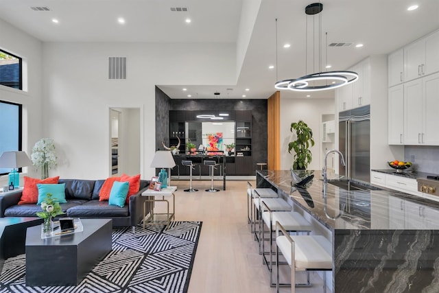 interior space with sink, high end refrigerator, white cabinets, dark stone counters, and light wood-type flooring