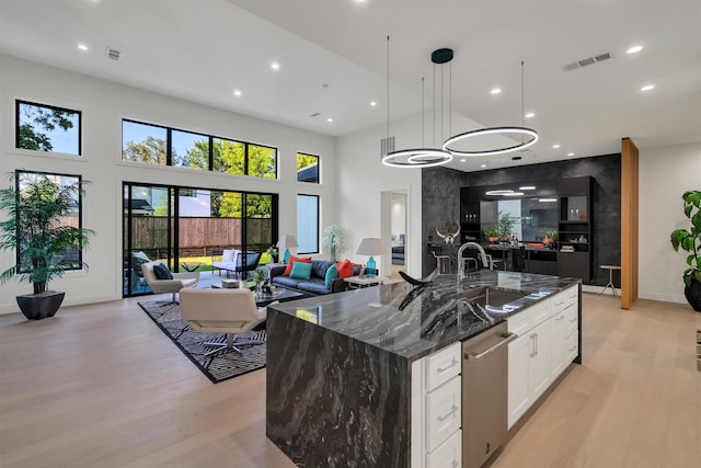 kitchen featuring white cabinetry, light wood-type flooring, dark stone countertops, pendant lighting, and a large island