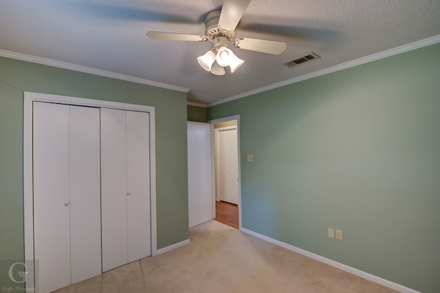 unfurnished bedroom with a textured ceiling, a closet, ornamental molding, light colored carpet, and ceiling fan