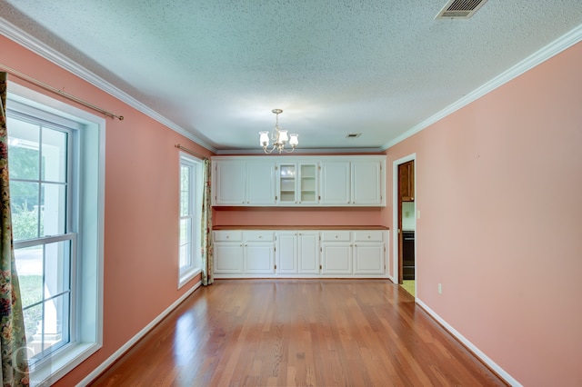 interior space featuring plenty of natural light, ornamental molding, light wood-type flooring, and a chandelier