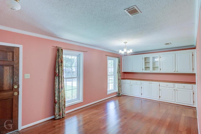 interior space featuring visible vents, ornamental molding, a textured ceiling, a chandelier, and light wood-type flooring