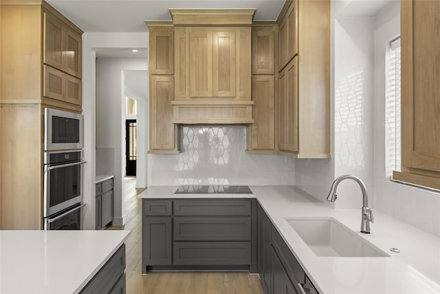 kitchen with black electric stovetop, stainless steel microwave, sink, light wood-type flooring, and decorative backsplash