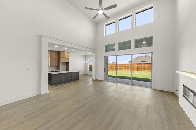 981 Stanford Ln, Prosper, TX 75078 - unfurnished living room featuring a towering ceiling, light wood finished floors, a ceiling fan, baseboards, and a glass covered fireplace