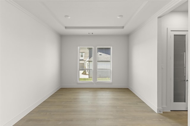 spare room with light hardwood / wood-style floors, crown molding, and a raised ceiling