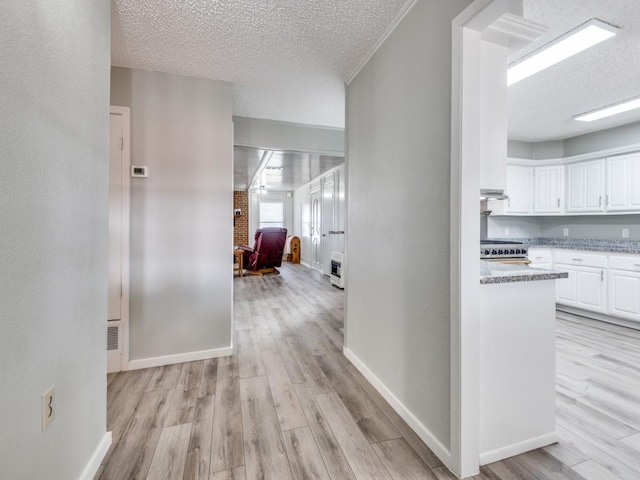 hall featuring light wood-style flooring, baseboards, and a textured ceiling