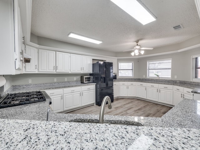 kitchen featuring white cabinets, light wood-type flooring, black fridge, ceiling fan, and a textured ceiling