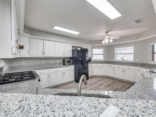 kitchen featuring light wood-type flooring, white cabinets, black refrigerator with ice dispenser, and gas range oven