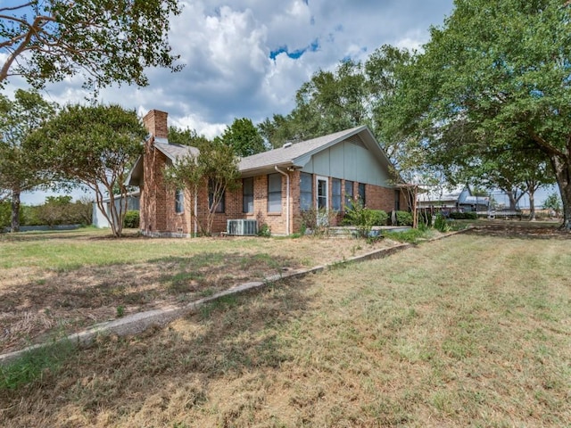 view of front of home with central air condition unit, a chimney, a front lawn, and brick siding