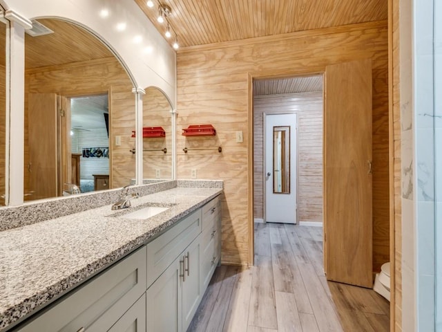 bathroom featuring wooden ceiling, wood walls, wood finished floors, vanity, and rail lighting