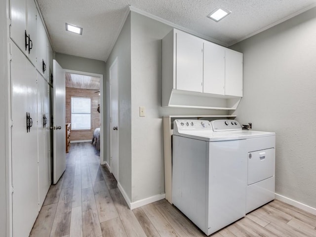 laundry area featuring cabinet space, light wood finished floors, baseboards, a textured ceiling, and washer and dryer