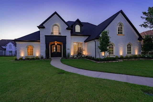 french country inspired facade with a yard, brick siding, and french doors