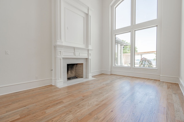 unfurnished living room with light wood-style floors, a fireplace, a towering ceiling, and baseboards