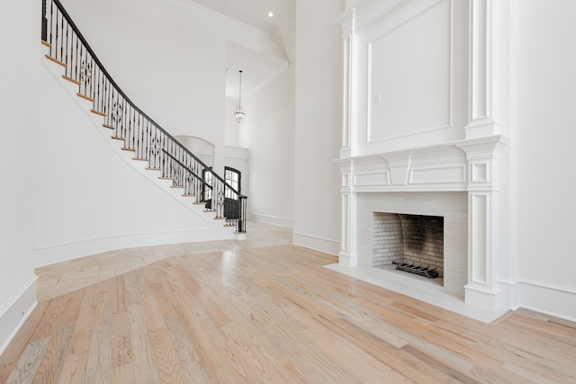 unfurnished living room with light wood-type flooring, crown molding, and a towering ceiling