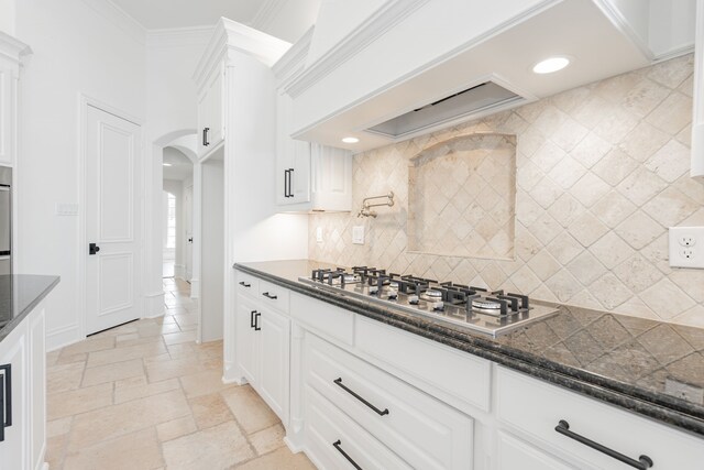 kitchen with backsplash, appliances with stainless steel finishes, crown molding, dark stone countertops, and white cabinets