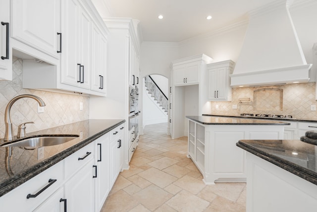 kitchen featuring arched walkways, custom exhaust hood, stone tile flooring, ornamental molding, and a sink