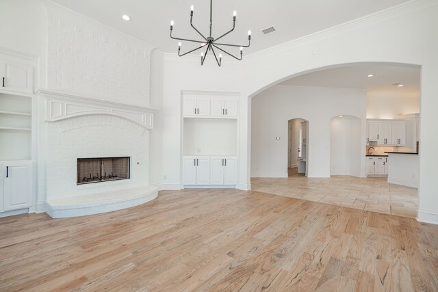 unfurnished living room with ornamental molding, light hardwood / wood-style flooring, an inviting chandelier, and a fireplace