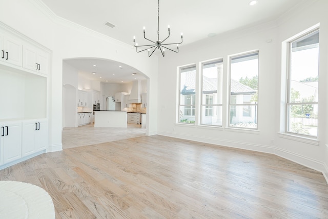 unfurnished living room with arched walkways, light wood-style flooring, visible vents, ornamental molding, and an inviting chandelier