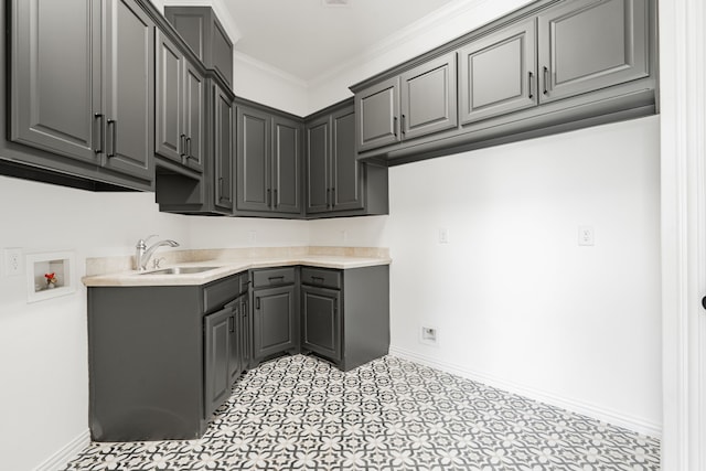 kitchen with crown molding, gray cabinets, a sink, and baseboards