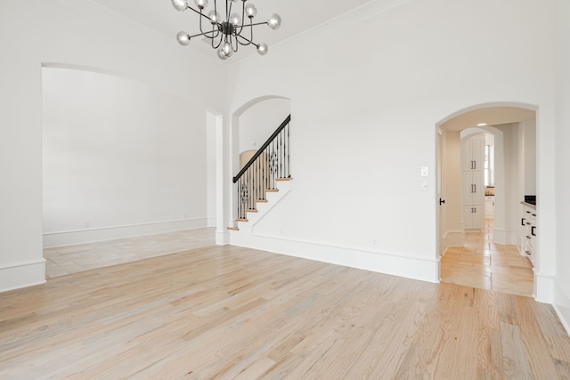 unfurnished living room with crown molding, a high ceiling, an inviting chandelier, and light wood-type flooring