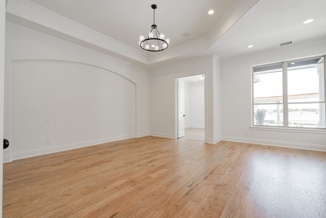 empty room featuring ornamental molding, a tray ceiling, an inviting chandelier, and light hardwood / wood-style floors