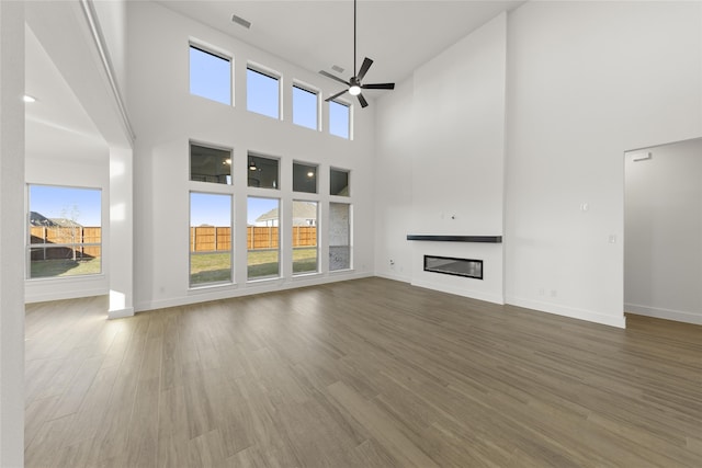 unfurnished living room featuring a towering ceiling, hardwood / wood-style flooring, and ceiling fan