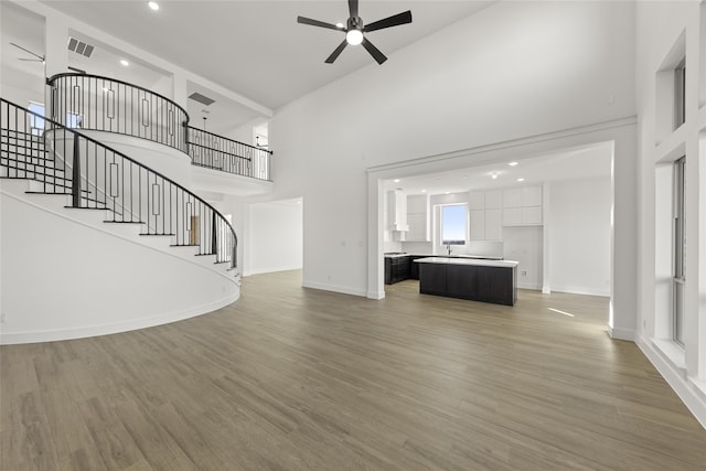 unfurnished living room with a high ceiling, ceiling fan, and hardwood / wood-style floors