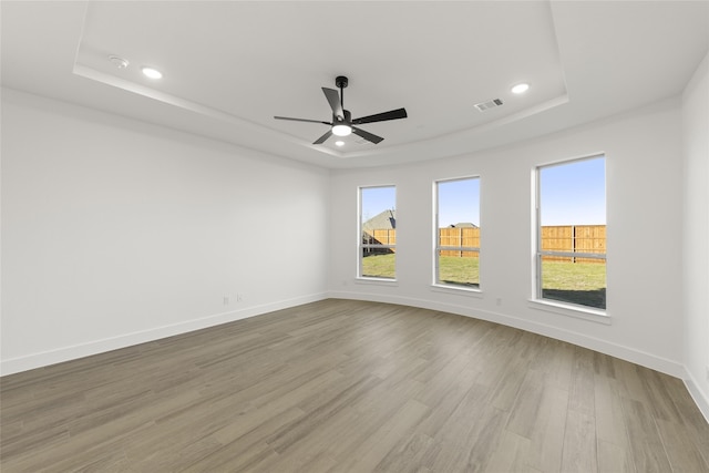 unfurnished room with a tray ceiling, ceiling fan, and light hardwood / wood-style flooring