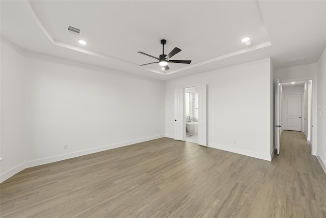 unfurnished room featuring light wood-type flooring, a tray ceiling, and ceiling fan