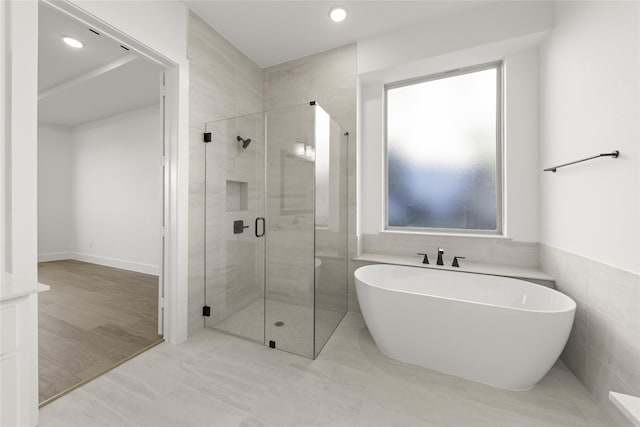 bathroom with shower with separate bathtub and tile walls