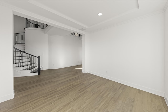 empty room featuring a raised ceiling, wood-type flooring, and ornamental molding